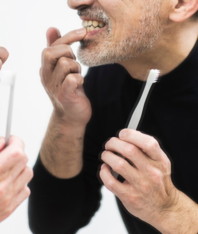 Photo d un homme se touchant les dents en tenant une brosse a dents dans l autre main j ai les dents qui bougent | Dr Monsenego & Fils Asnieres sur Seine